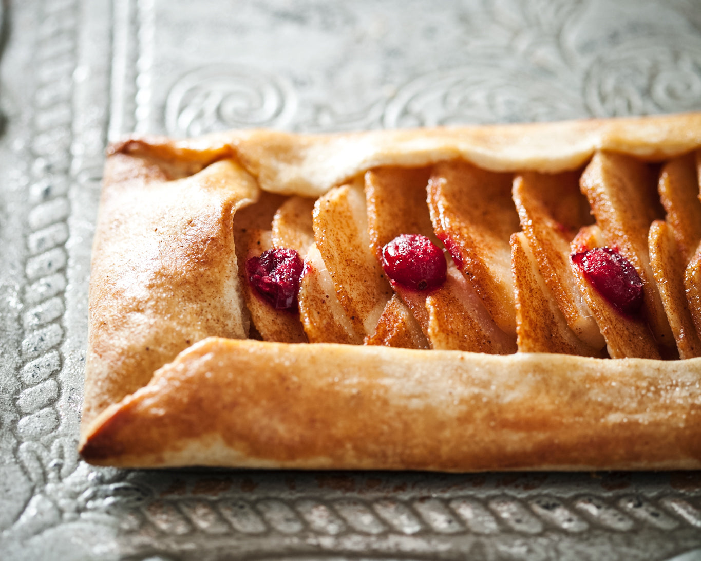 Pear tart with cranberries on a textured silver tray