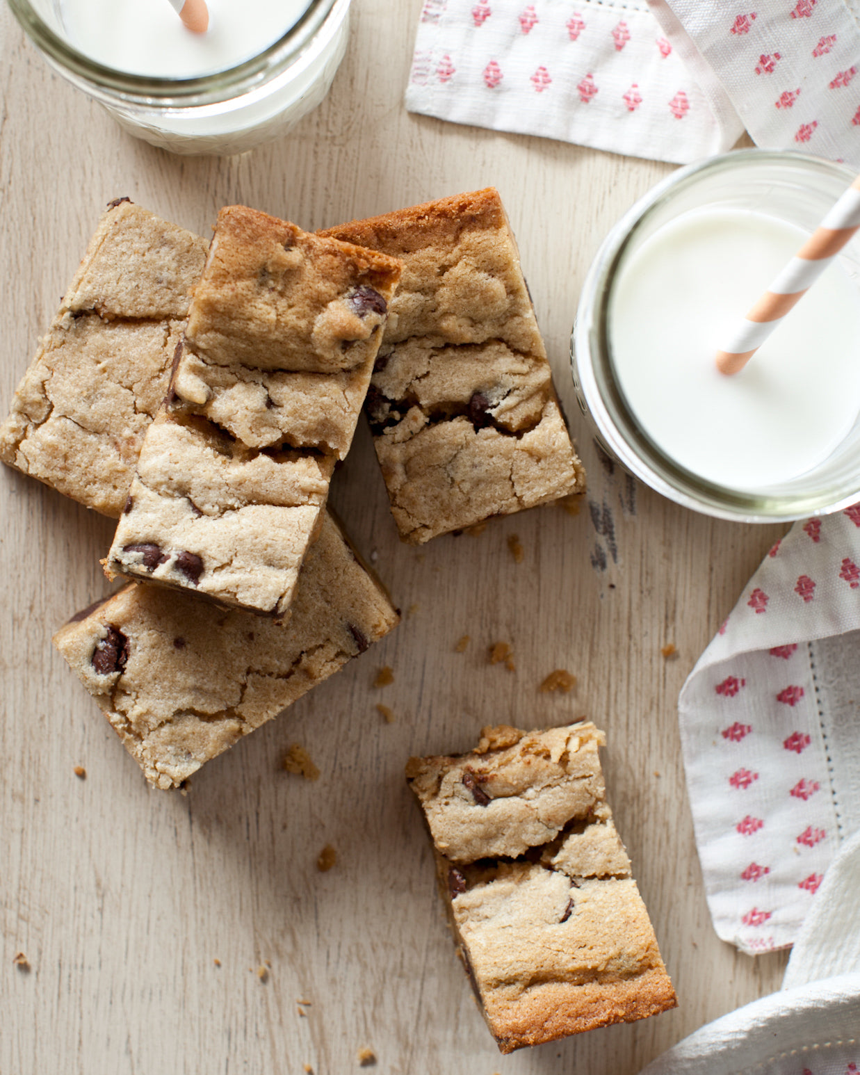 Rectangular peanut butter blondie bars with chocolate chips on a wooden surface with glasses of milk.